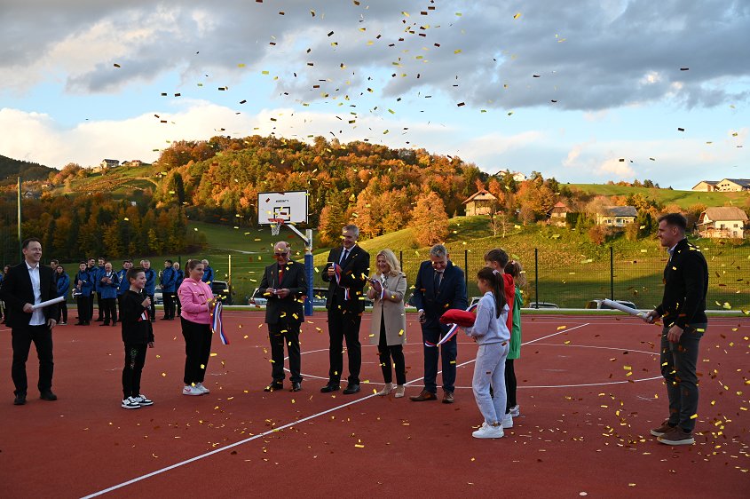 Na igrišču so v družbi osnovnošolcev gostje prerezali trak, spuščeni pa so bili zlati konfeti. Na fotografiji so gostje z deli traku, v zraku pa letijo zlati konfeti. 
